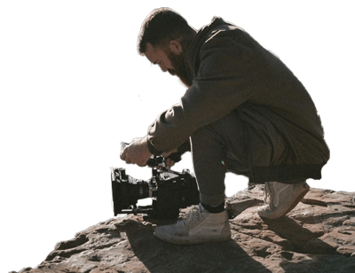 un homme utilisant une caméra pour faire un reportage en haut d'un rocher.